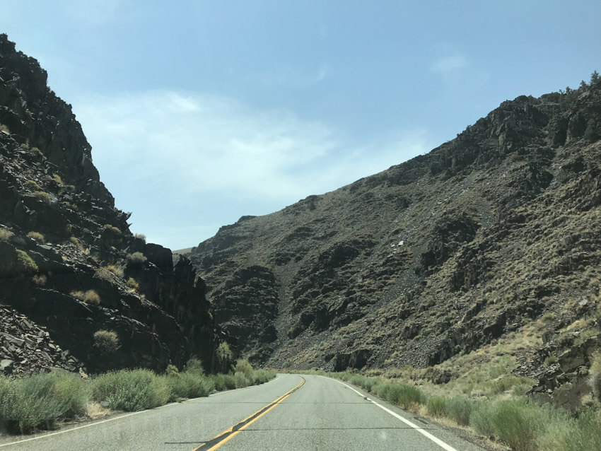 A stretch of road curving slightly to the left, with dark-coloured high rock on the sides of the road.