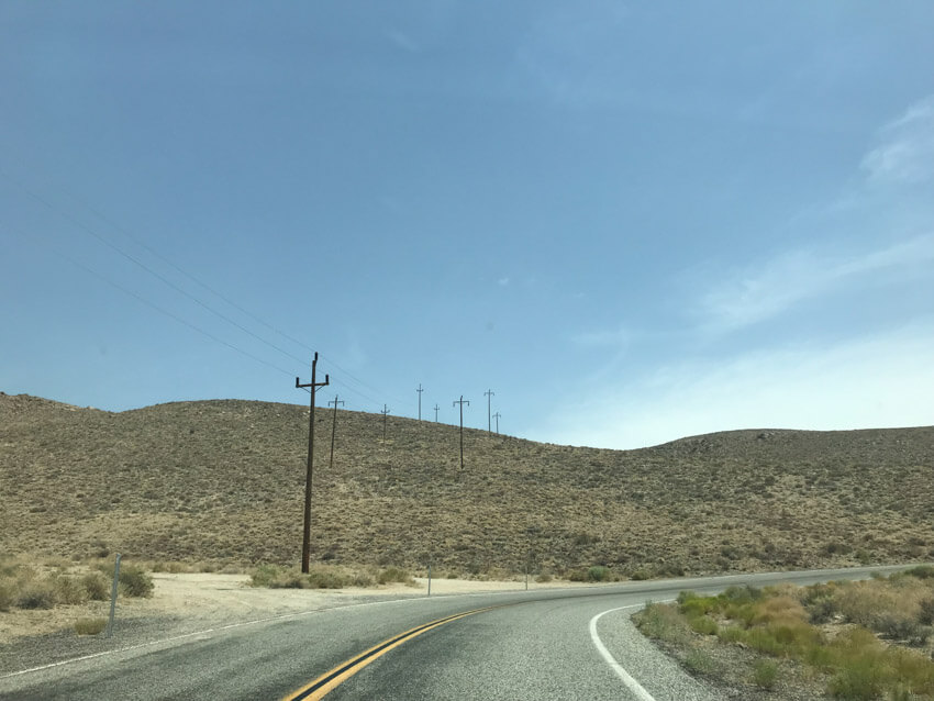 A stretch of road turning to the right. There are power poles on the left side and they connect to each other via thin power lines.