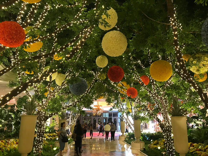 Fake trees adorned with fairy lights and large baubles made of flowers, forming a canopy over an internal marble floor