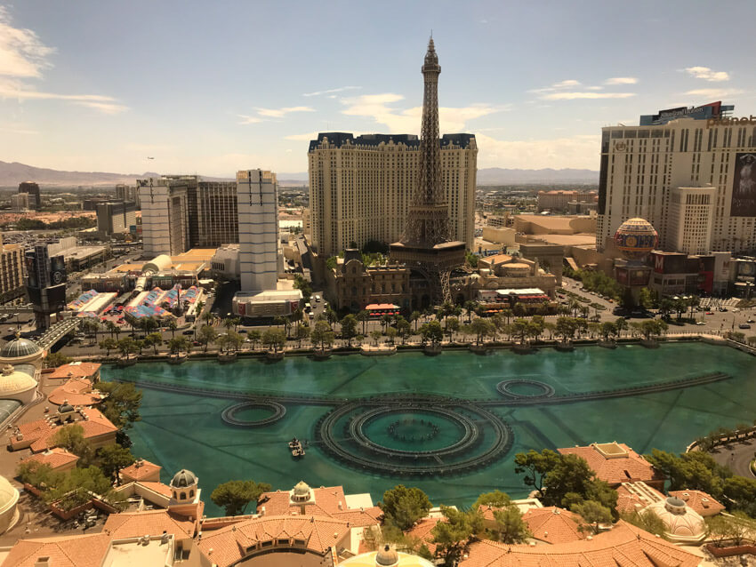 A daytime view of a large fountain arrangement in a body of water, with an Eiffel Tower replica and other tall buildings in the background