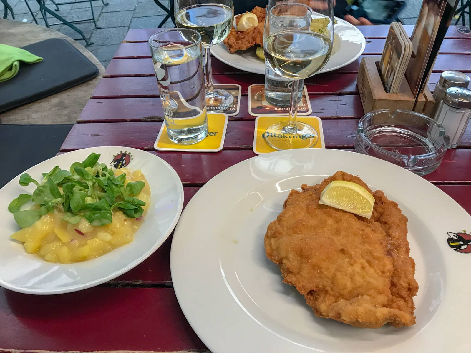 Two plates on a table, one with potato salad and the other with schnitzel and a lemon on top