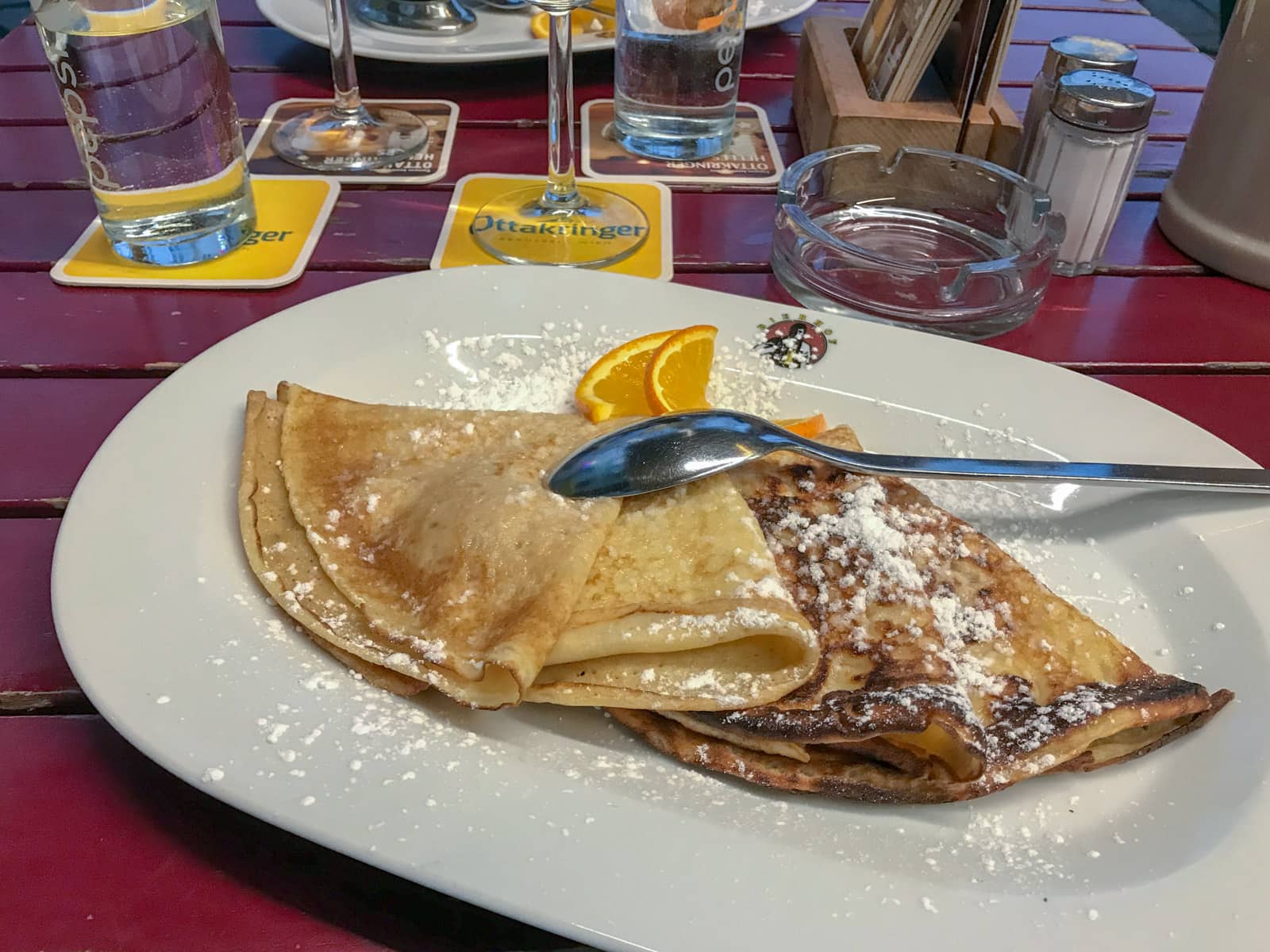 Folded pancakes on a plate drizzled with icing sugar