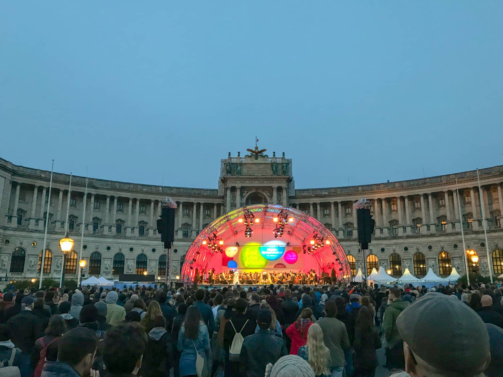 A crowd gathered in front of an outdoor stage lit up with colourful lights