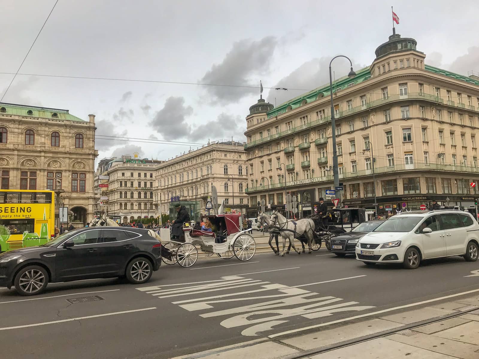 A busy street in Vienna with cars, a bus, and a horse carriage on the road.