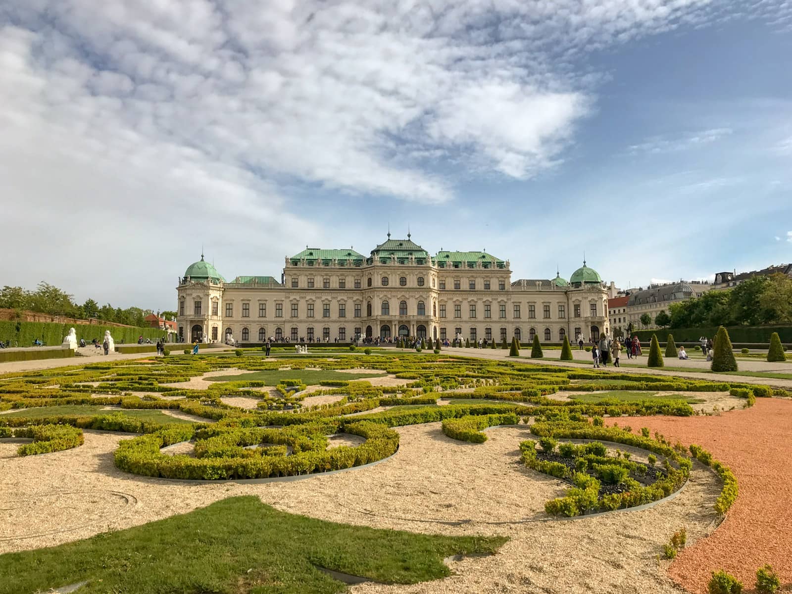 The Schössgarten grounds, with short hedges making a swirly pattern on the lawn in the foreground. There is a streak of white clouds across the sky