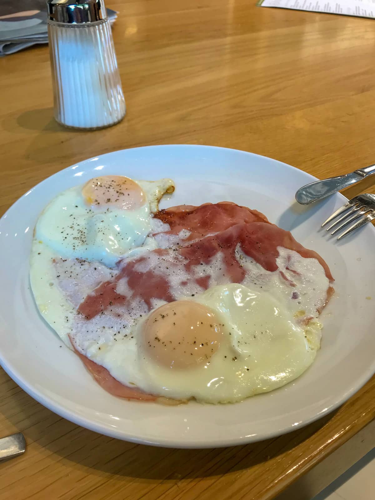 A white plate with some fried eggs and ham, seasoned with pepper