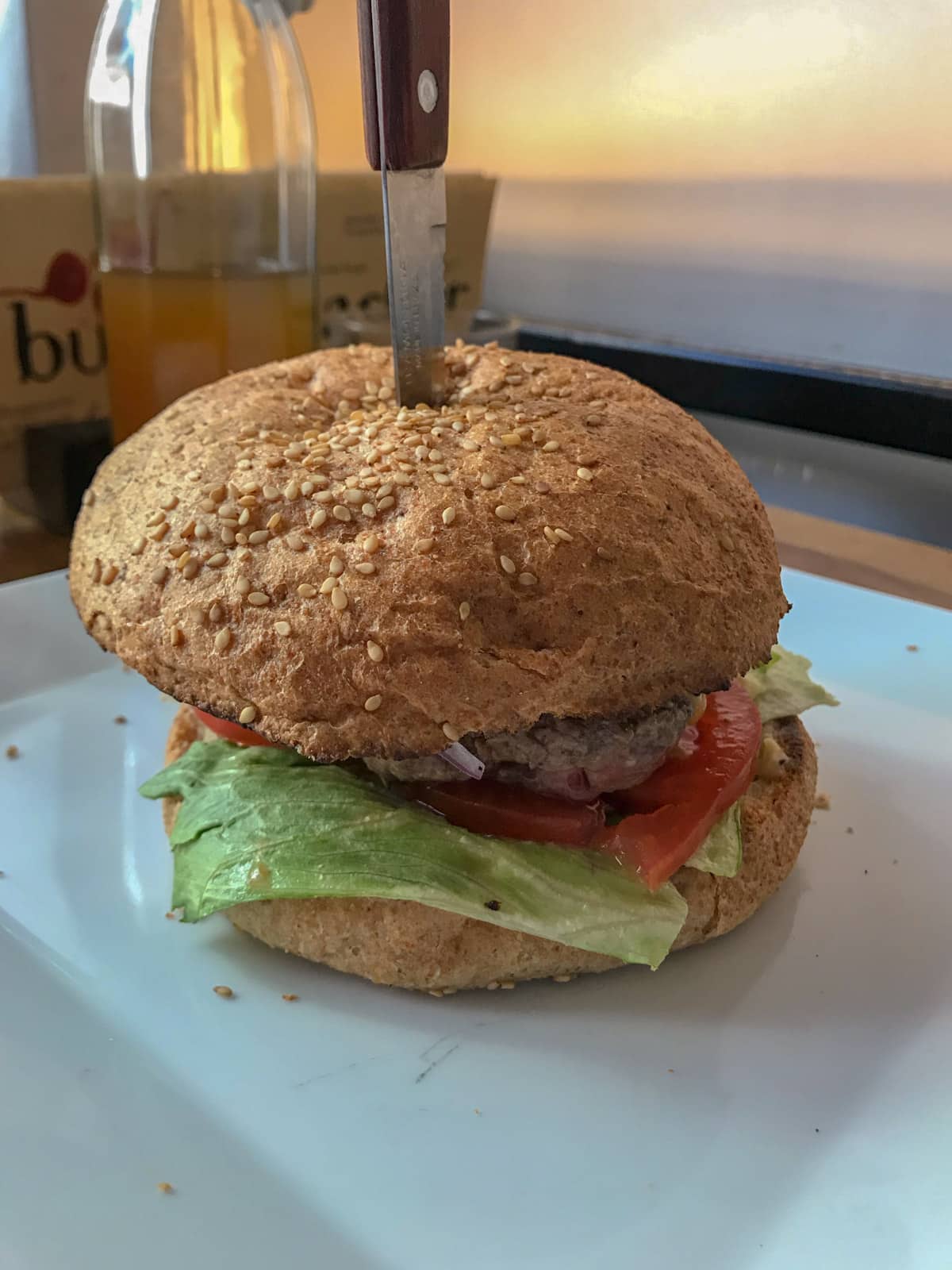 A beef burger on a white plate. It has a knife through the top of it.