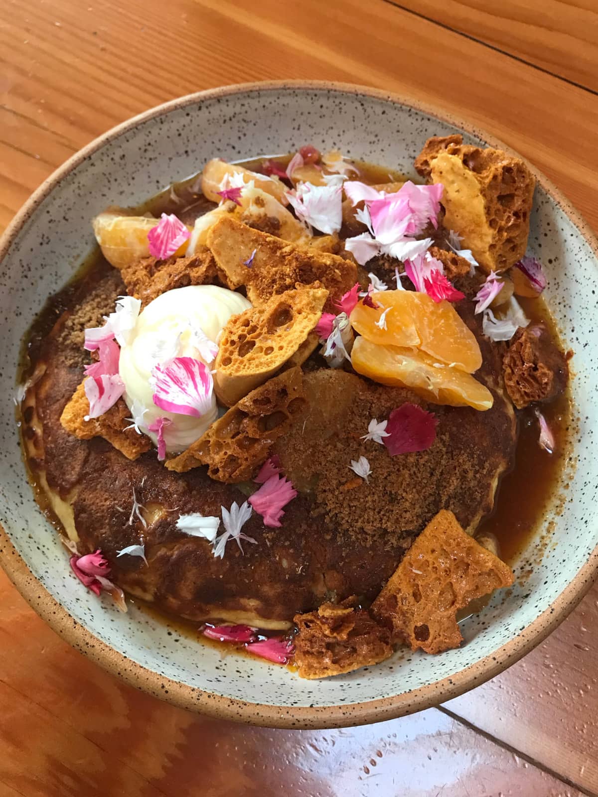 A bowl with hotcakes, decorated with flowers and served with citrus fruit and honeycomb