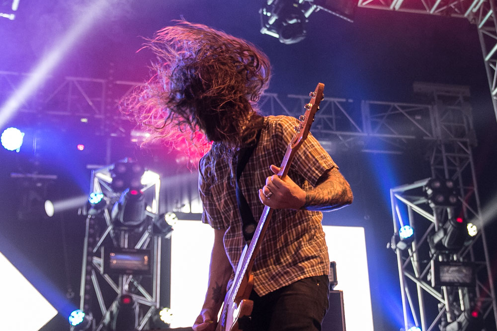 A man on stage playing a guitar, his long hair obscuring his whole face