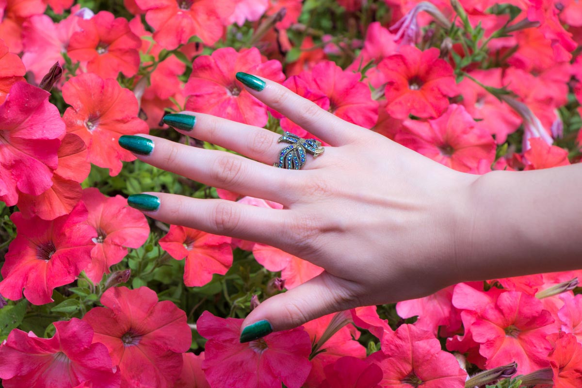 My outstretched hand with a feather ring and dark green sparkly painted nails