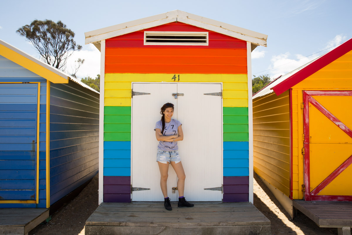Me standing in front of a hut with all the colours of the rainbow.
