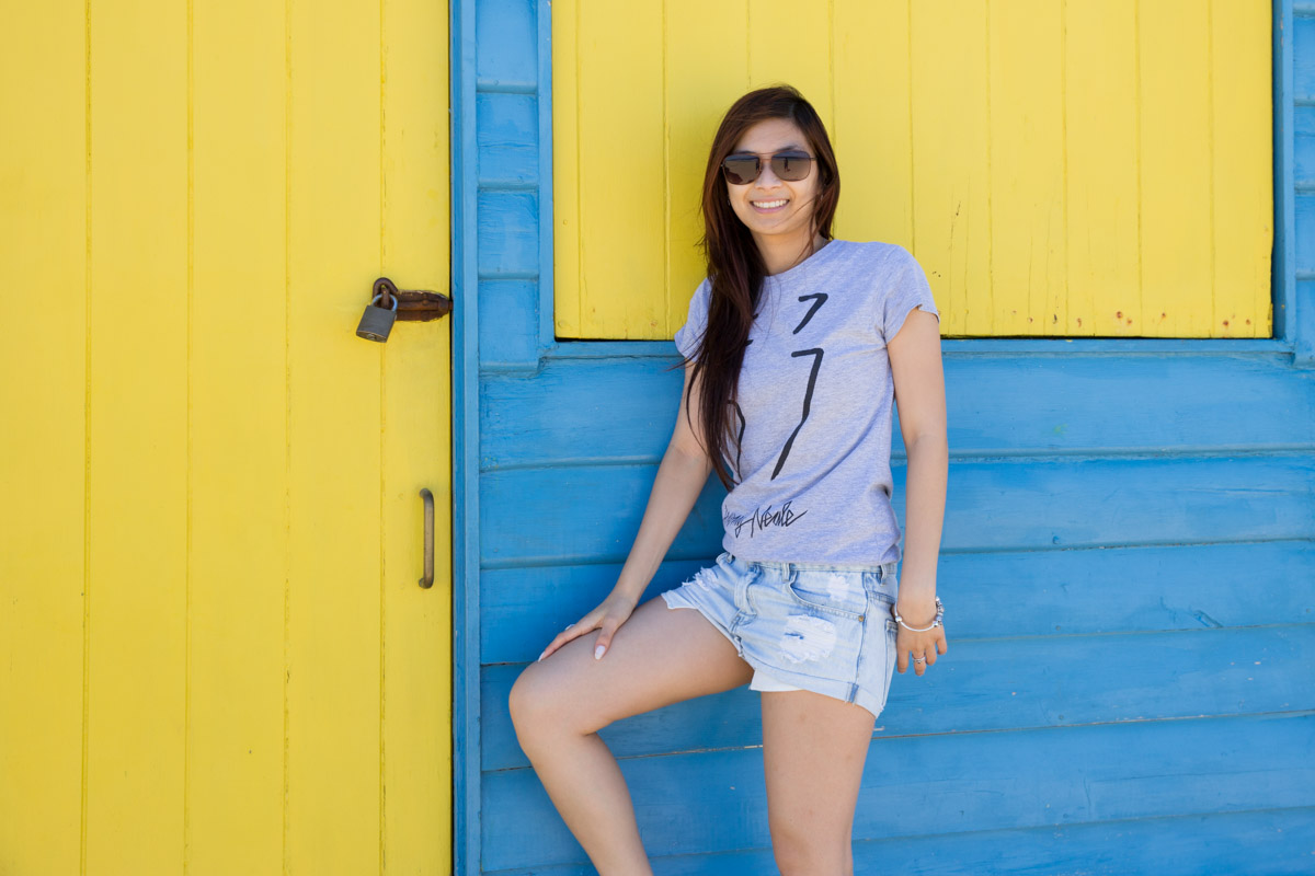 Leaning against a blue hut with a yellow door and window